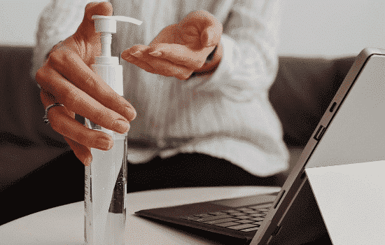 closeup of employee using hand sanitizer by computer in compliance with COVID-19 workplace guidance