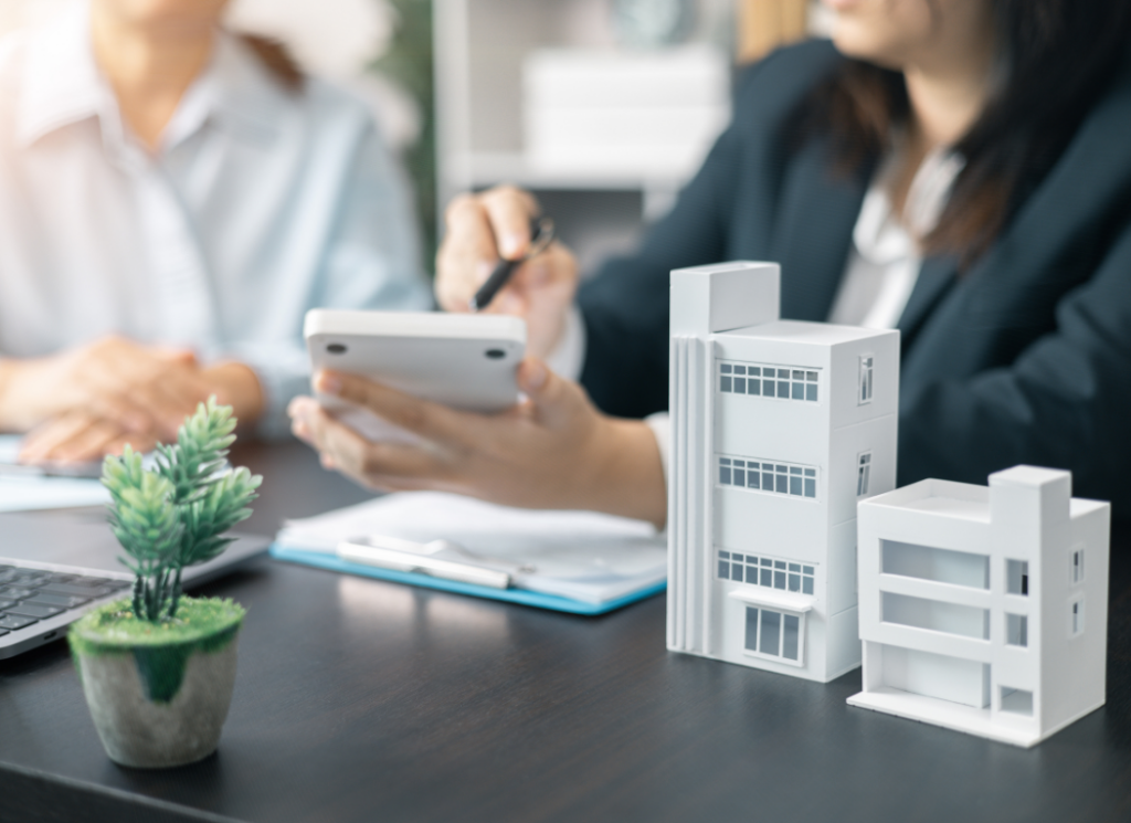An accountant with a calculator and clipboard sits at a desk with miniature building models and reviews available real estate tax credits with a real estate fund investor.