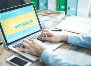 A laptop computer sits open on an office desk. An outsourced HR professional is typing on the laptop and the word 