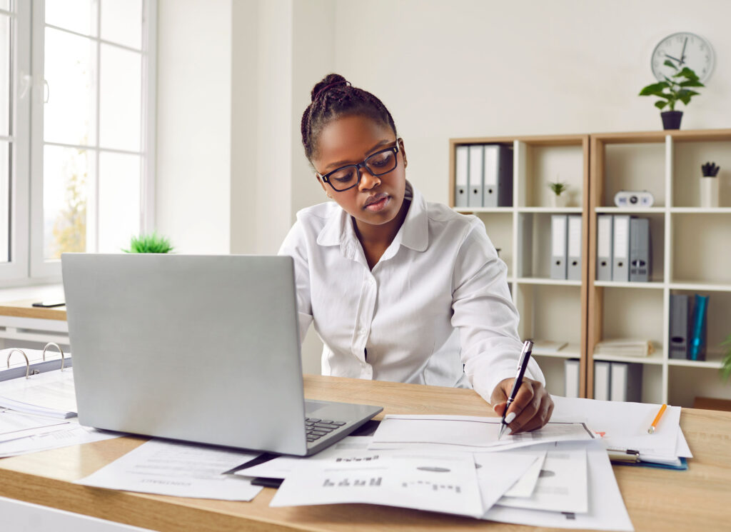 Woman with glasses is sitting at her desk in front of a laptop monitor in the office. Automated NCAA and EADA reporting