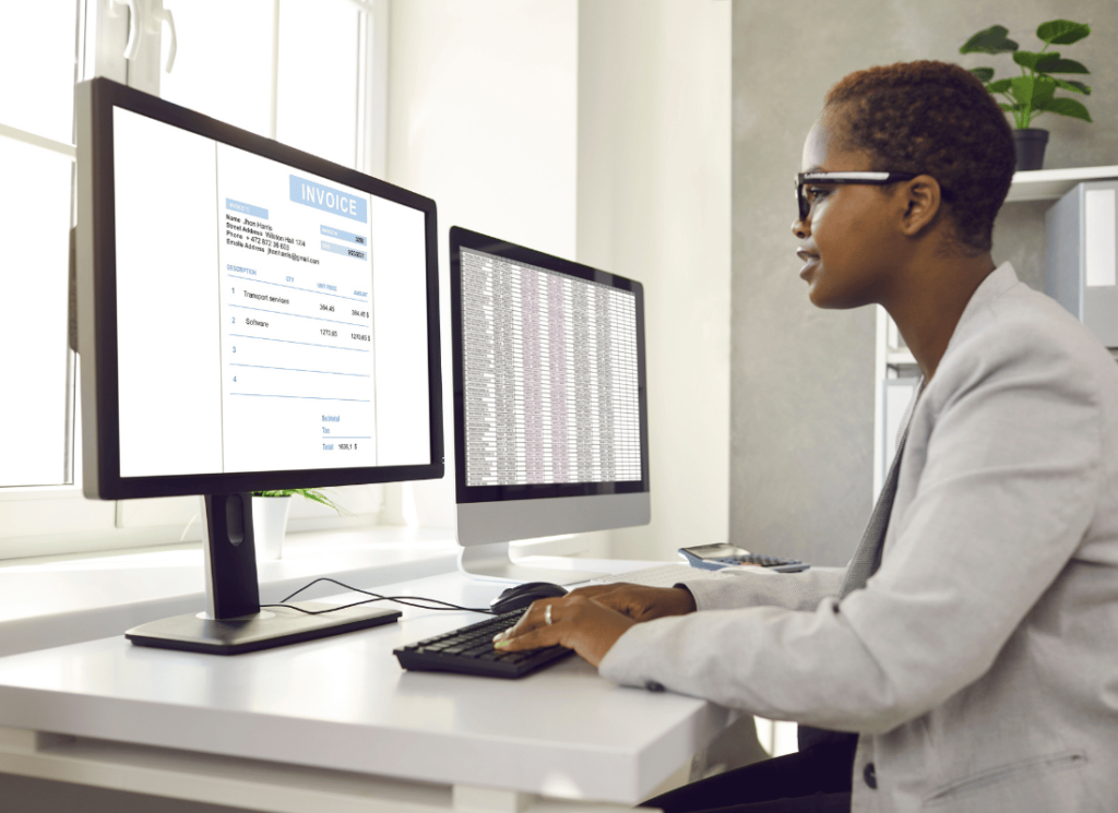 An accountant is sitting at a computer desk with dual monitors and using an accounting software to review financial data.