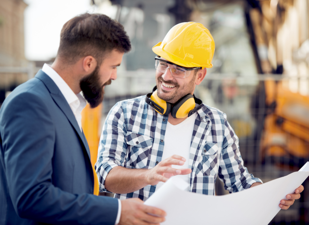 A construction worker, wearing a hardhat and safety glasses is discussing plans with a construction CPA and consultant wearing business attire.