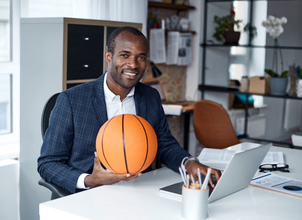 A university athletics business office professional holding a basketball at a desk, symbolizing the value of outsourced business office support in sports management and administration.