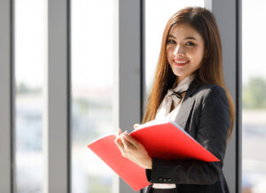 Smiling woman standing wearing black suit, Businesswoman holding employee handbook in office room.