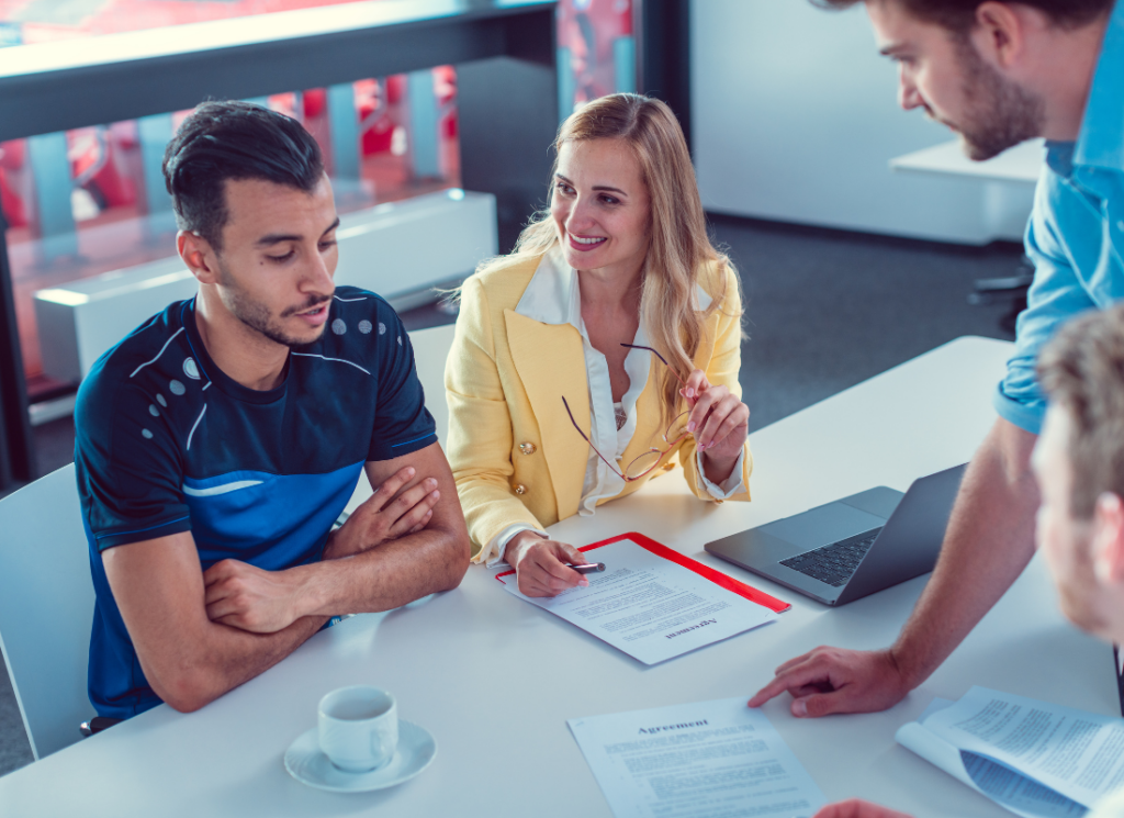 College athlete and business representatives discussing contract in NIL agreements, symbolizing the evolving landscape of multimedia rights and revenue sharing in college athletics