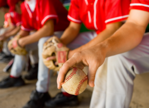 A college baseball team sitting on a bench, highlighting the changes to maximum roster sizes in college athletics.