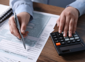 Close-up of a tax accountant using a calculator while filling out tax forms, representing the process of calculating and filing for Employee Retention Credits (ERC).