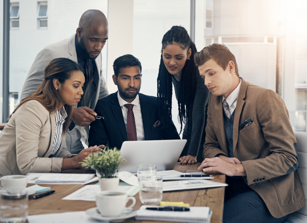 A group of tax professionals in business attire gather around a laptop, engaged in a focused discussion on R&D tax credits.