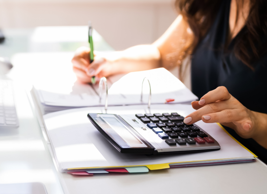 A business professional is using a calculator while taking notes in a binder filled with organized documents. The scene conveys a focus on tax preparation and tax credits.