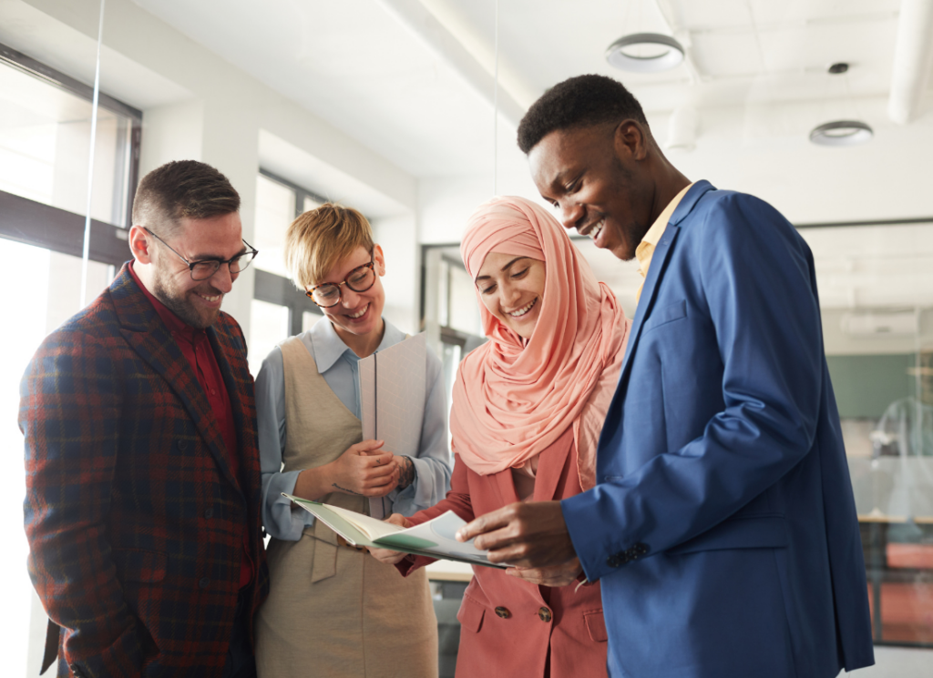 A diverse group of professionals smile as they review a document together in a bright office setting.