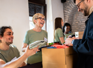 A group of cheerful volunteers distributes goods and interacts with people at a charity event.