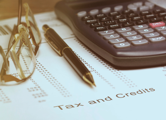 A close-up of a calculator, pen, and glasses resting on a document labeled "Tax and Credits."