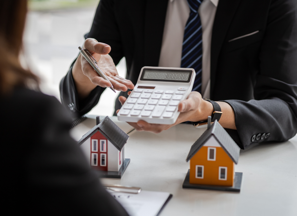 A real estate professional explains tax calculations with a calculator and model houses on a desk, illustrating passive activity rules in real estate tax.