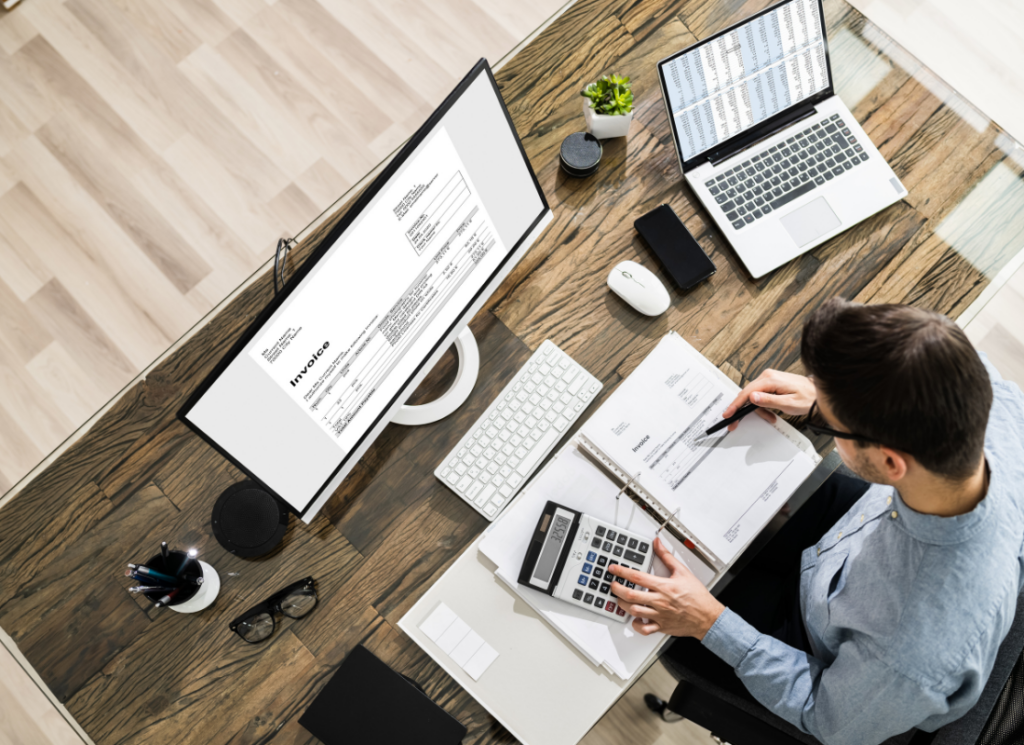 A real estate investor reviews invoices and financial documents with a calculator at a desk preparing for year-end tax planning.