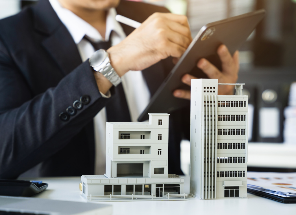 A real estate developer holding a tablet with scale models of buildings on a desk, representing real estate tax planning.