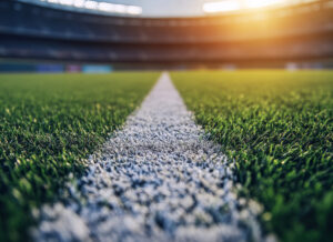 Close-up view of a college football field with a white line running through the grass under a bright stadium light,.