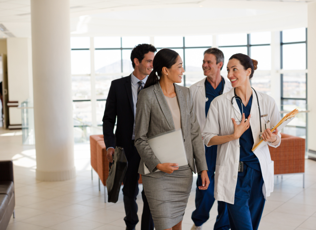 A group of physicians and business professionals walk together in a modern medical facility, in a discussion about selling a medical practice to private equity.