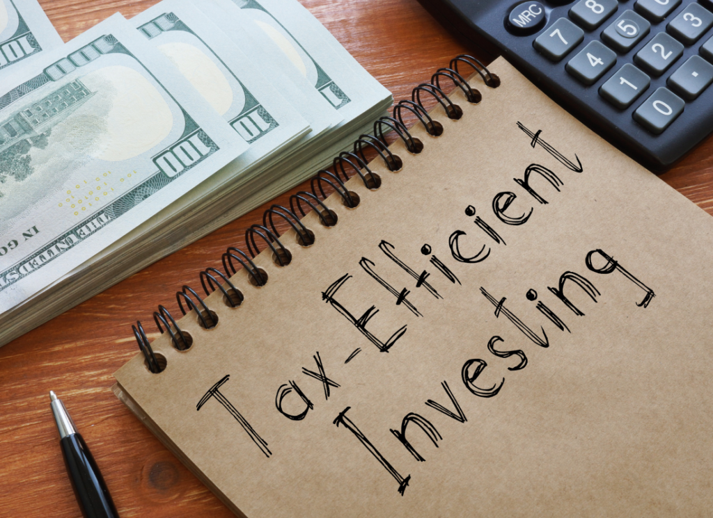 A notepad with 'Tax-Efficient Investing' written on it, accompanied by a stack of hundred-dollar bills, a pen, and a calculator, symbolizing financial planning and investment strategies.