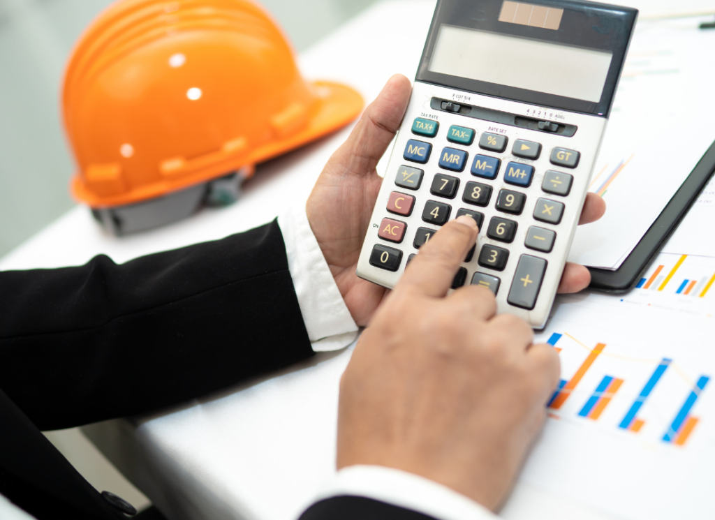 A construction accountant using a calculator with financial charts and an orange construction helmet on the table, representing the fundamentals of construction accounting.