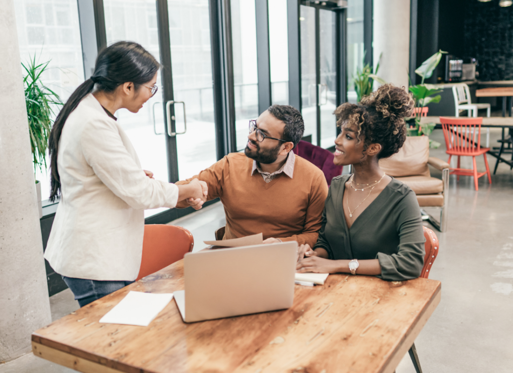 A financial advisor shakes hands with a couple during an estate planning consultation in a modern office setting.