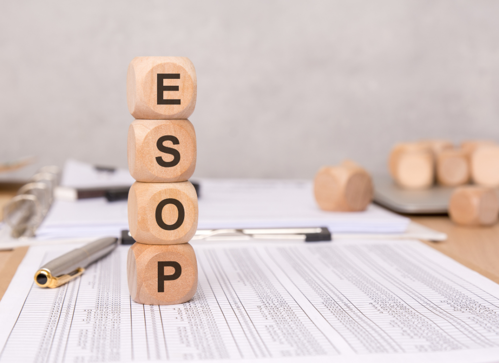 Wooden blocks stacked to spell "ESOP" sit on financial documents, with a pen and binder nearby, symbolizing employee stock ownership plans in the construction industry.