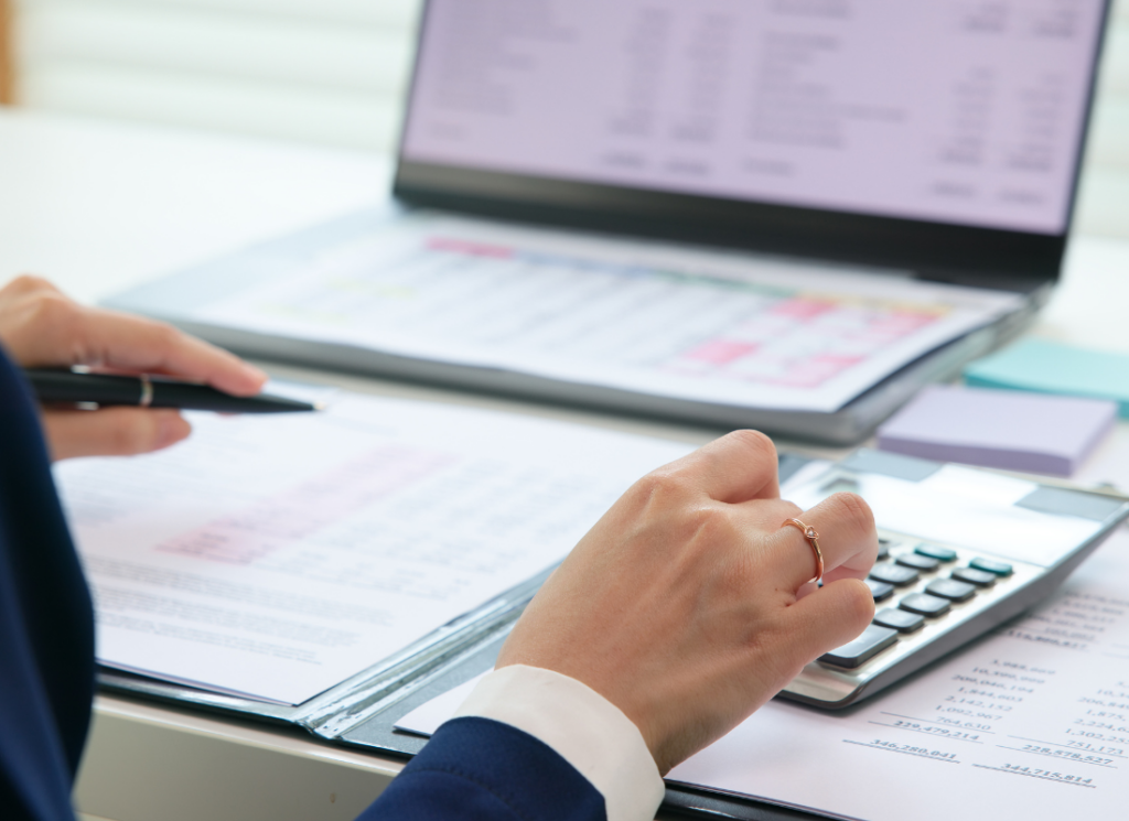 A professional reviews financial documents, using a calculator while analyzing data on a laptop. The image represents specialized government financial services.