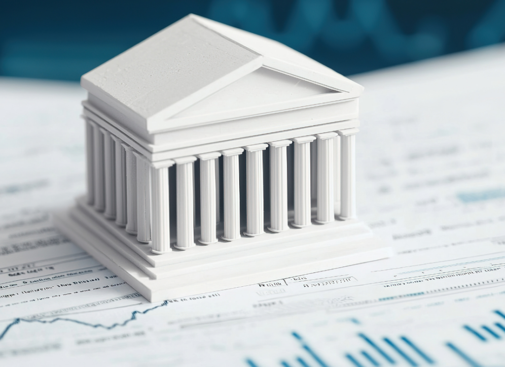 A small white model of a government building with columns sits on financial documents featuring charts and graphs, symbolizing outsourced finance in government.