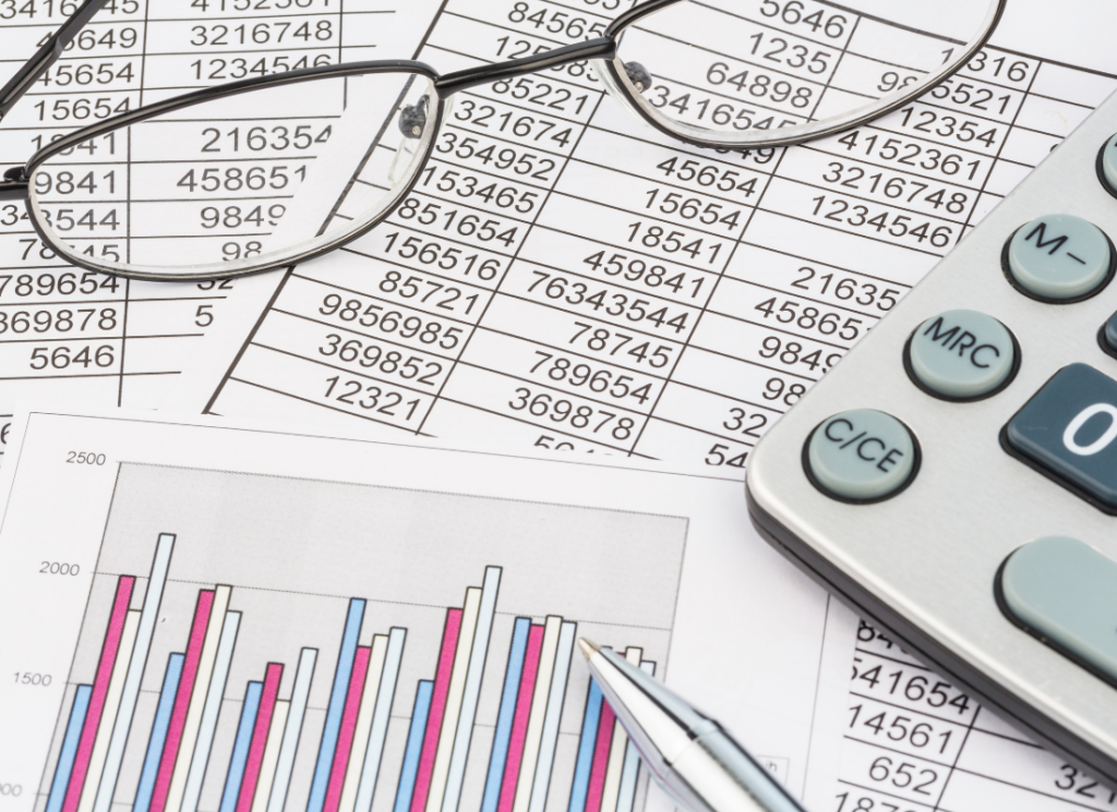 A calculator, glasses, and a pen rest on financial spreadsheets with numerical data and bar graphs, symbolizing analysis, planning, and financial strategy.